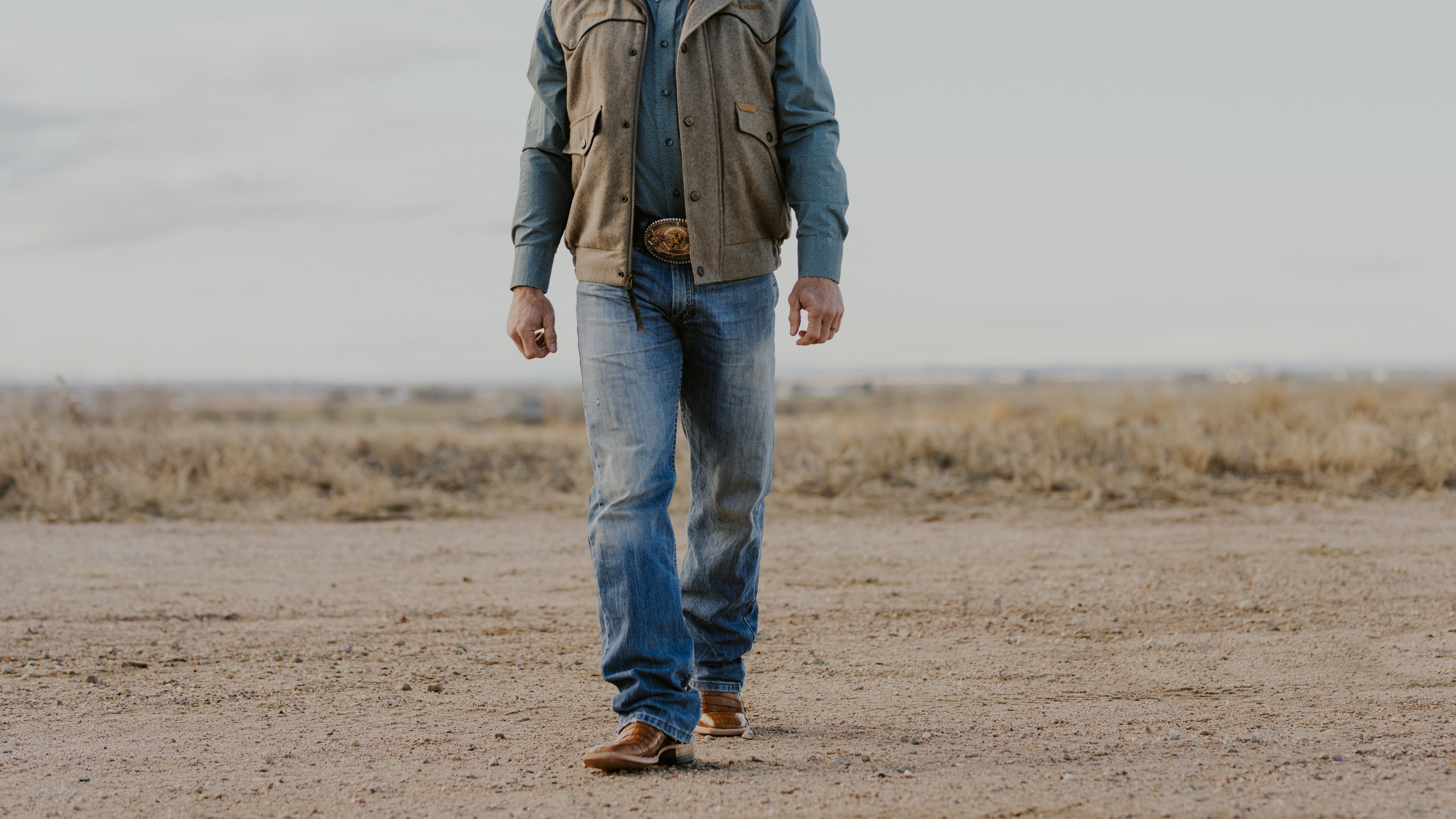 Man in cowboy hat and vest standing in a desert landscape